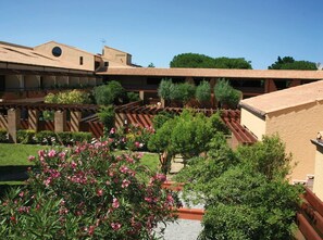 Ein Innenhof mit einer Pergola, Kübelpflanzen und einem Gebäude mit Ziegeldach.