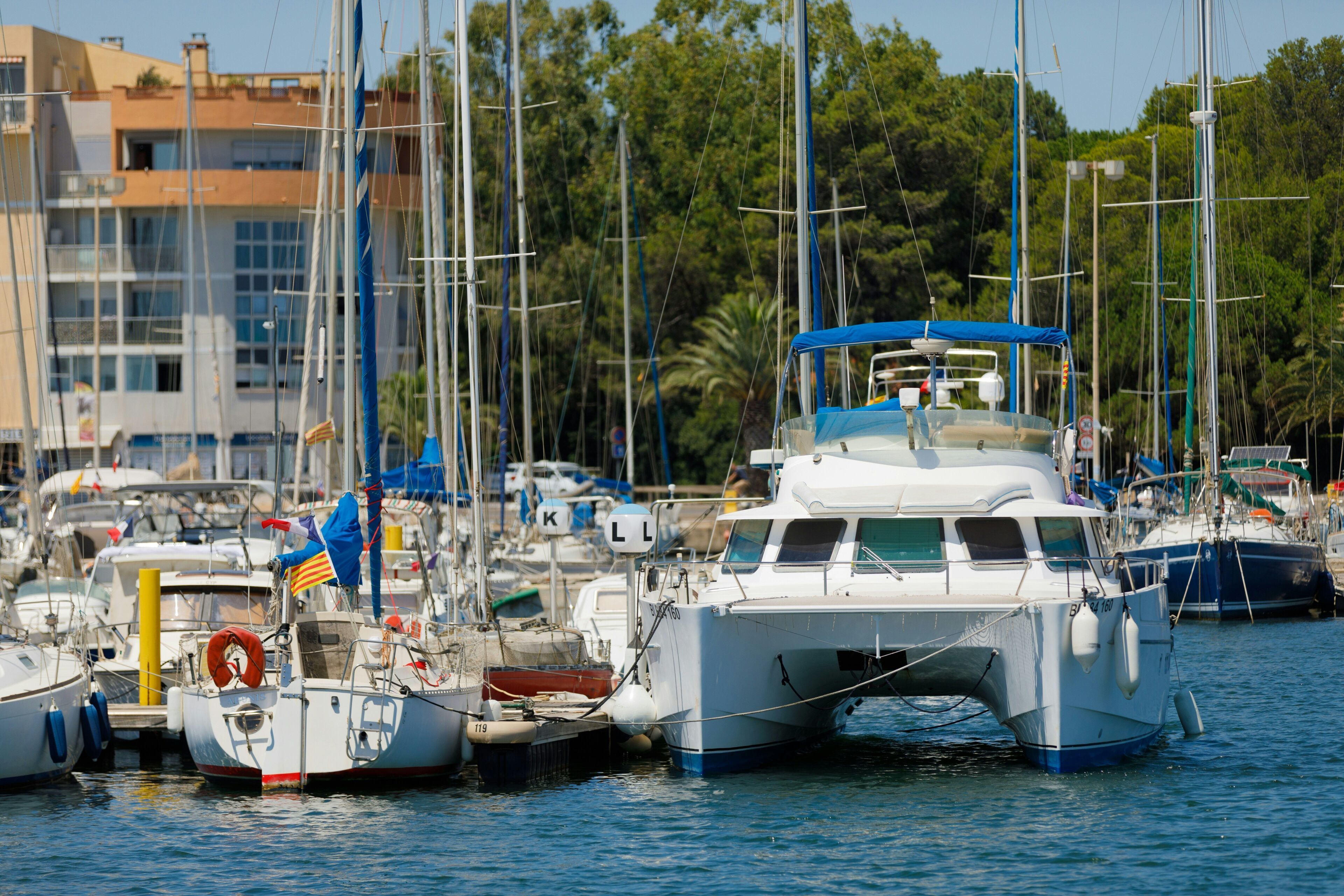 A marina with various boats docked, a building with multiple windows in the background, and a clear sky.