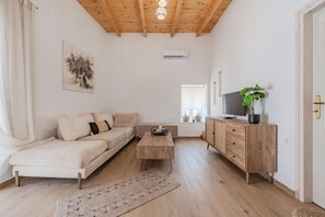 Ein modernes Wohnzimmer mit Holzboden, einer Couch, einem Couchtisch, einem Fernseher auf einer Holzkommode und einer Pflanze.