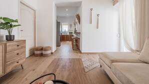Ein Wohnzimmer mit einer Couch, Holzboden, einer Pflanze, einem Schrank und einer Küche im Hintergrund.