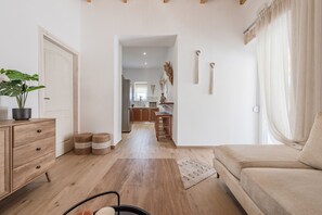 Ein Wohnzimmer mit einer Couch, Holzboden, einer Pflanze, einem Schrank und einer Küche im Hintergrund.