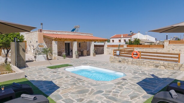 A pool area with stone flooring, lounge chairs, and a small building with a red roof. - Olea Holiday House (Rethymno)