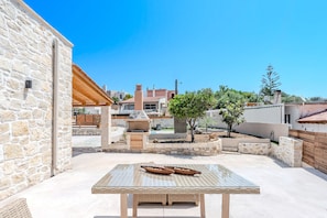 Ein Steinhaus mit einer Pergola, einem Tisch im Freien und einer Grillgelegenheit.