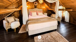 A cozy attic bedroom with a large bed, a chair, and a small table. - Cabanas da Mata - Alfredo Wagner - SC (Arnópolis)