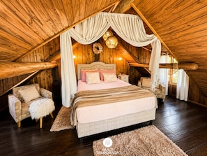 A cozy attic bedroom with a large bed, a chair, and a small table.