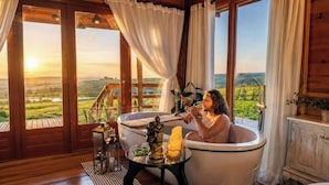 A room with a bathtub, a table with candles, and a view of the countryside. - Cabanas da Mata - Alfredo Wagner - SC (Arnópolis)