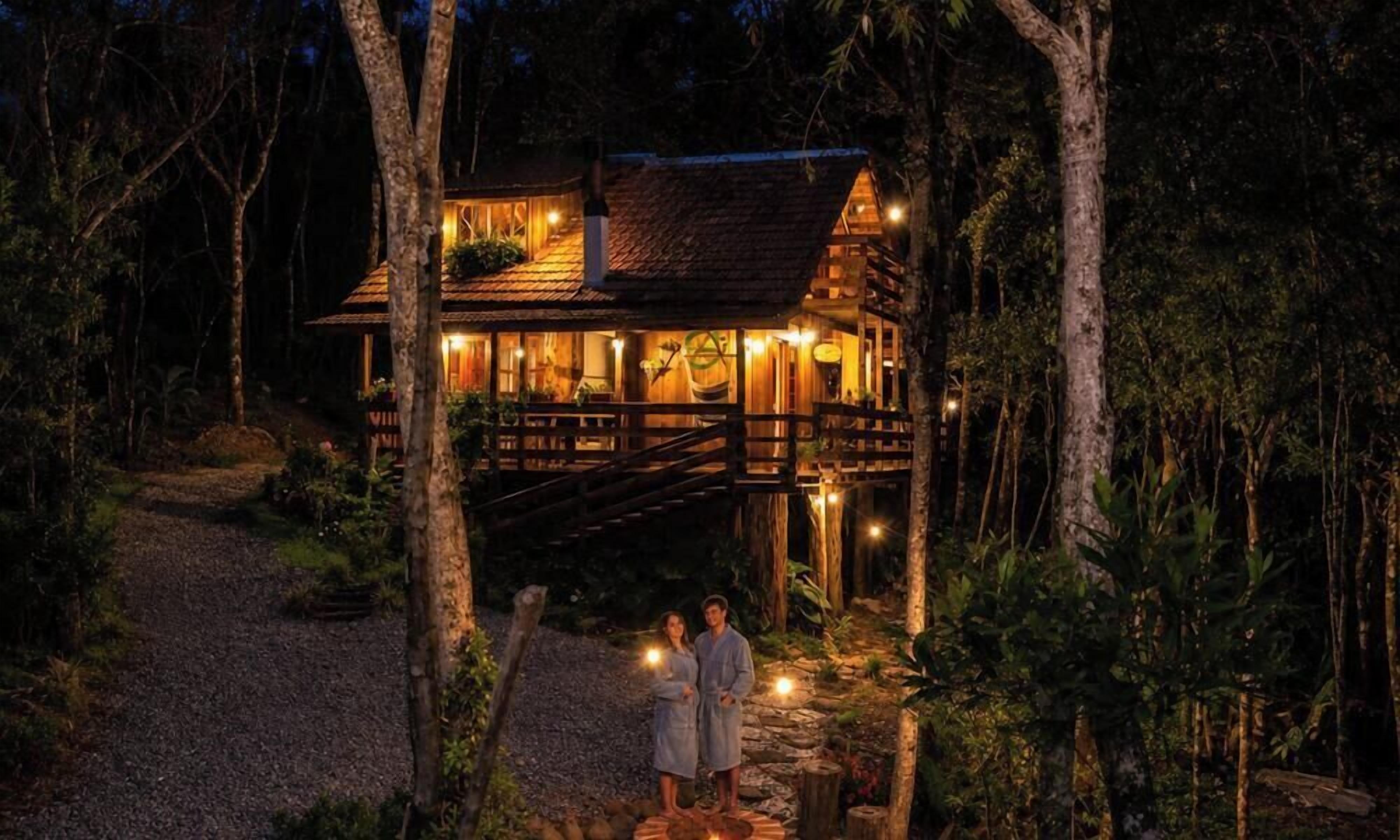 Uma cabana de madeira com varanda, cercada por árvores, à noite.