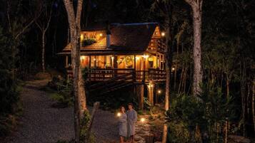 Uma cabana de madeira com varanda, cercada por árvores, à noite.