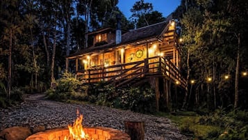 Eine Hütte mit Lagerfeuer, umgeben von einem Wald.