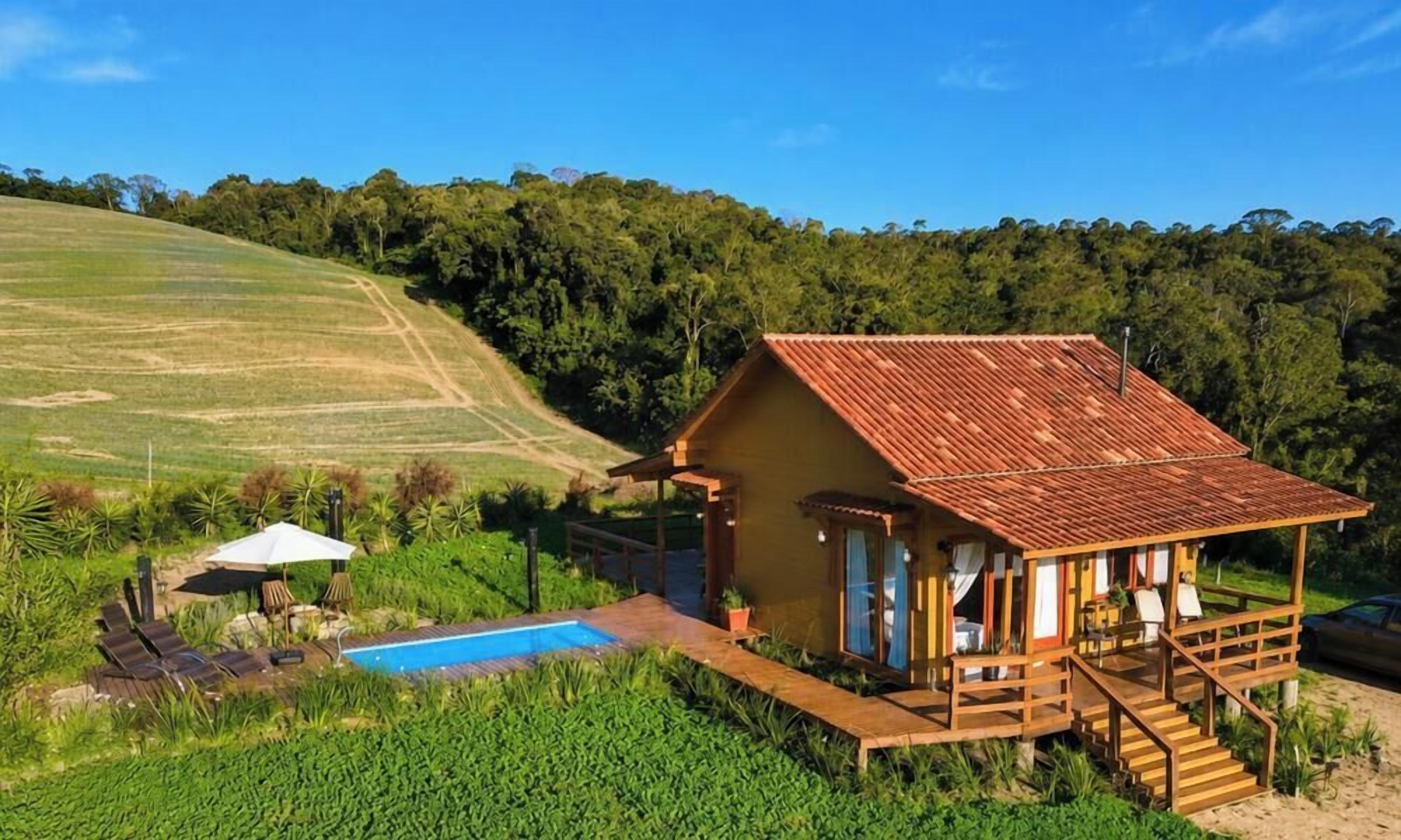 Una casa de madera rústica con piscina, rodeada de exuberante vegetación y un paisaje montañoso.
