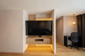 Ein modernes Wohnzimmer mit Flachbildfernseher, einer Holzunterhaltungsecke und einem schwarzen Bürostuhl.