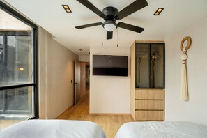 Ein Schlafzimmer mit Deckenventilator, Wand-Fernseher, Holzschrank und Fenster.