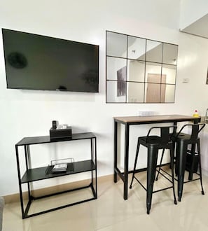 Ein modernes Zimmer mit Fernseher, einem Holzesstisch für zwei Personen, einer kleinen schwarzen Konsole und einem großen Spiegel an der Wand.