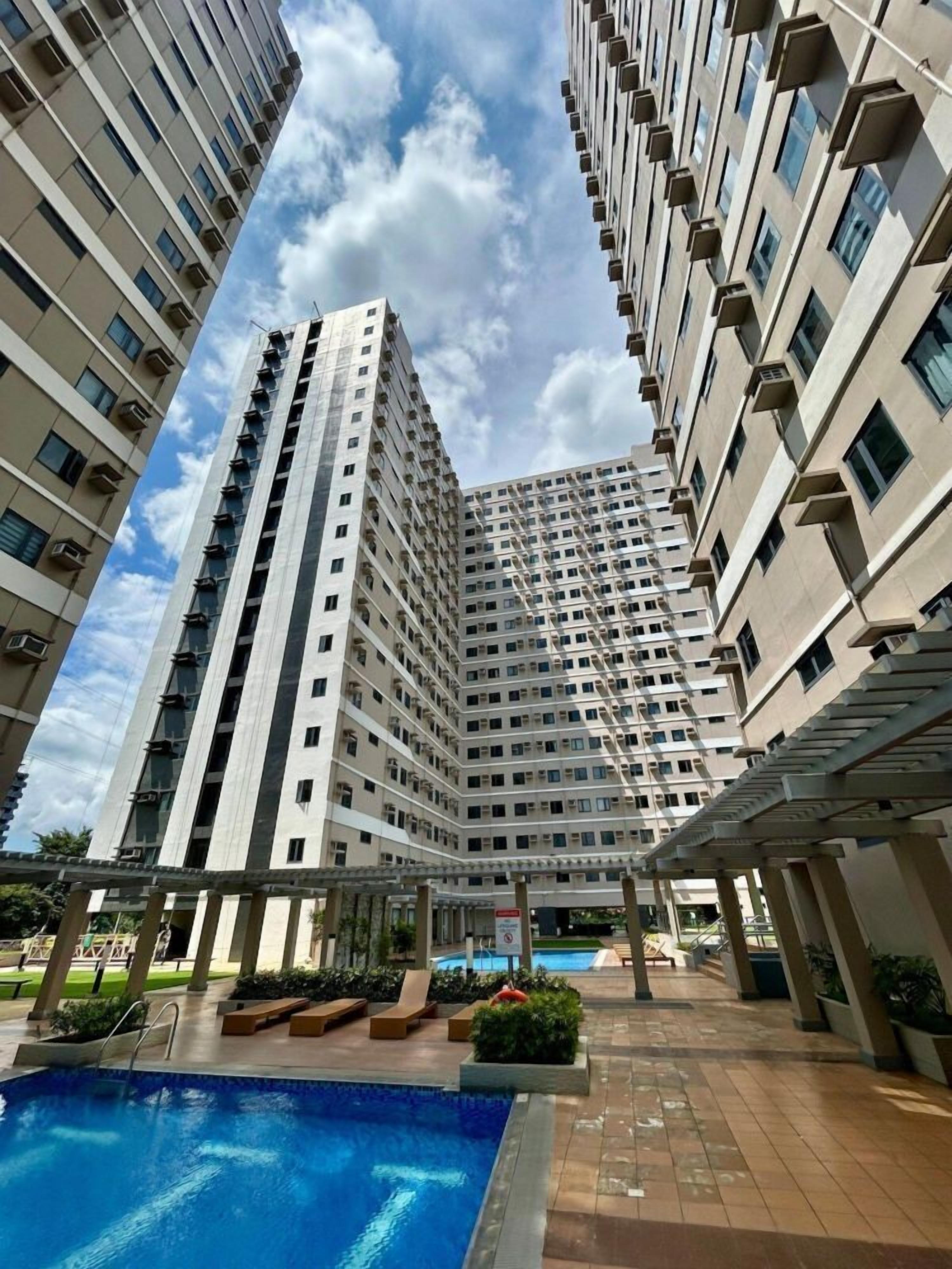 Un edificio residencial alto con múltiples balcones, una piscina y un área exterior cubierta con asientos.