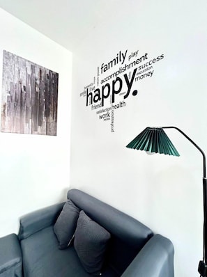 A room with a word cloud wall art, a gray sofa with patterned cushions, and a green lamp. - Your Perfect Dasmarinas Getaway (Dasmarinas)