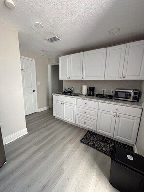 A compact kitchen with white cabinets, a microwave, and a coffee maker. - Home Away From Home – Holiday, FL (Holiday)