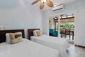 Ein Hotelzimmer mit zwei Betten, einem Deckenventilator, einer Klimaanlage und einem Balkon mit Sitzgelegenheiten.