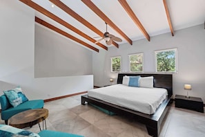 Ein modernes Schlafzimmer mit einem großen Bett, einem Deckenventilator und drei Fenstern.