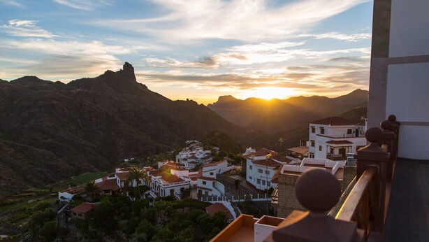 Un pueblo costero con edificios blancos, una montaña imponente y un atardecer.