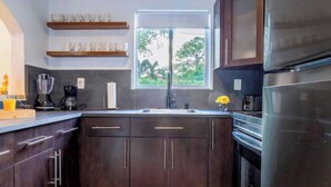 A modern kitchen with dark cabinets, a stainless steel refrigerator, and a window providing natural light. - Private Pool Oasis Near Wynwood, Midtown & Beaches (Miami)