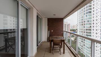 Un balcon avec une table et des chaises en bois, une porte vitrée et une vue sur des immeubles de grande hauteur.