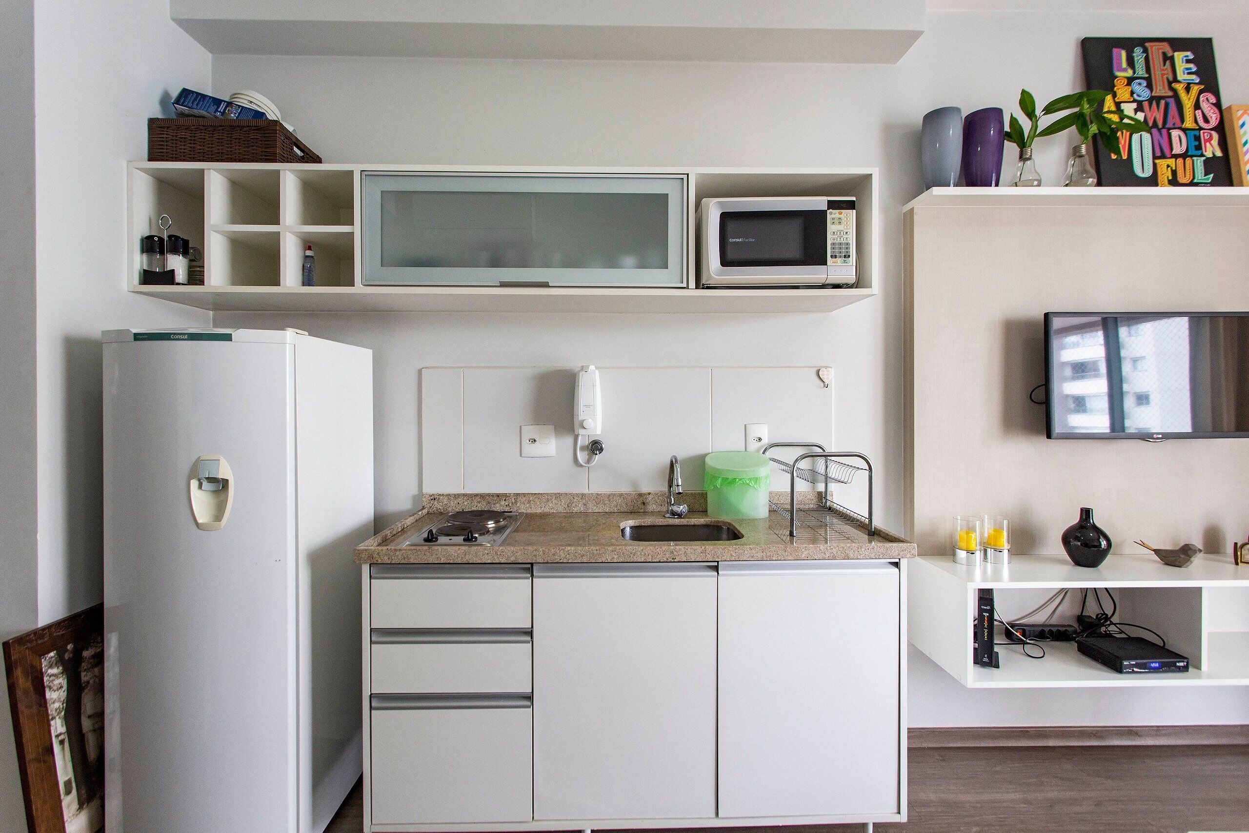 Eine kompakte Küche mit Kühlschrank, Mikrowelle, Spüle und einem wandmontierten Flachbildfernseher.