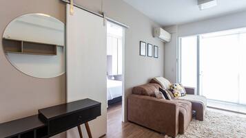 Une chambre moderne avec un lit, un canapé, un bureau, un miroir et une grande fenêtre.
