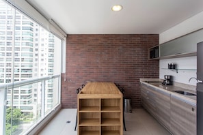 A small kitchen with a wooden table, a sink, and a view of a tall building through a window. - Affinity for Life (São Paulo)