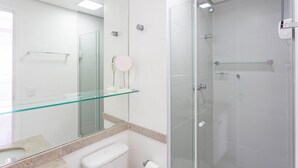 Un baño moderno con cabina de ducha de vidrio, repisa de vidrio sobre el lavamanos y un inodoro.
