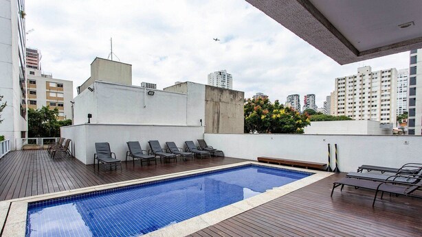 Una piscina al aire libre con sillas de descanso, una terraza de madera y vistas de edificios circundantes.