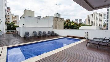 Une piscine extérieure avec des chaises longues, une terrasse en bois et une vue sur les bâtiments environnants.