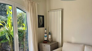 A room with a dining table, a sofa, a lamp, a nightstand, and a window with curtains. - The House with a Blue Garden and Ocean View (Monade Santa Lucia)