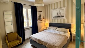 A bedroom with a bed, a chair, a window with curtains, a wall-mounted shelf, and a ceiling fan. - The House with a Blue Garden and Ocean View (Monade Santa Lucia)