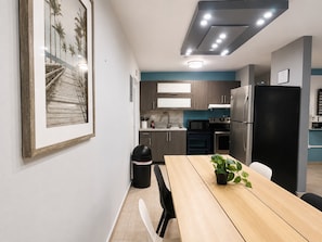 Eine moderne Küche mit dunklen Schränken, einem schwarzen Kühlschrank und einem Essbereich mit einem Holztisch und Stühlen.