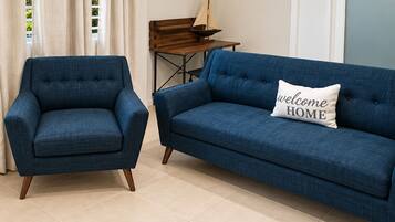 A living room with a blue armchair, a blue sofa, and a small table with a model sailboat.