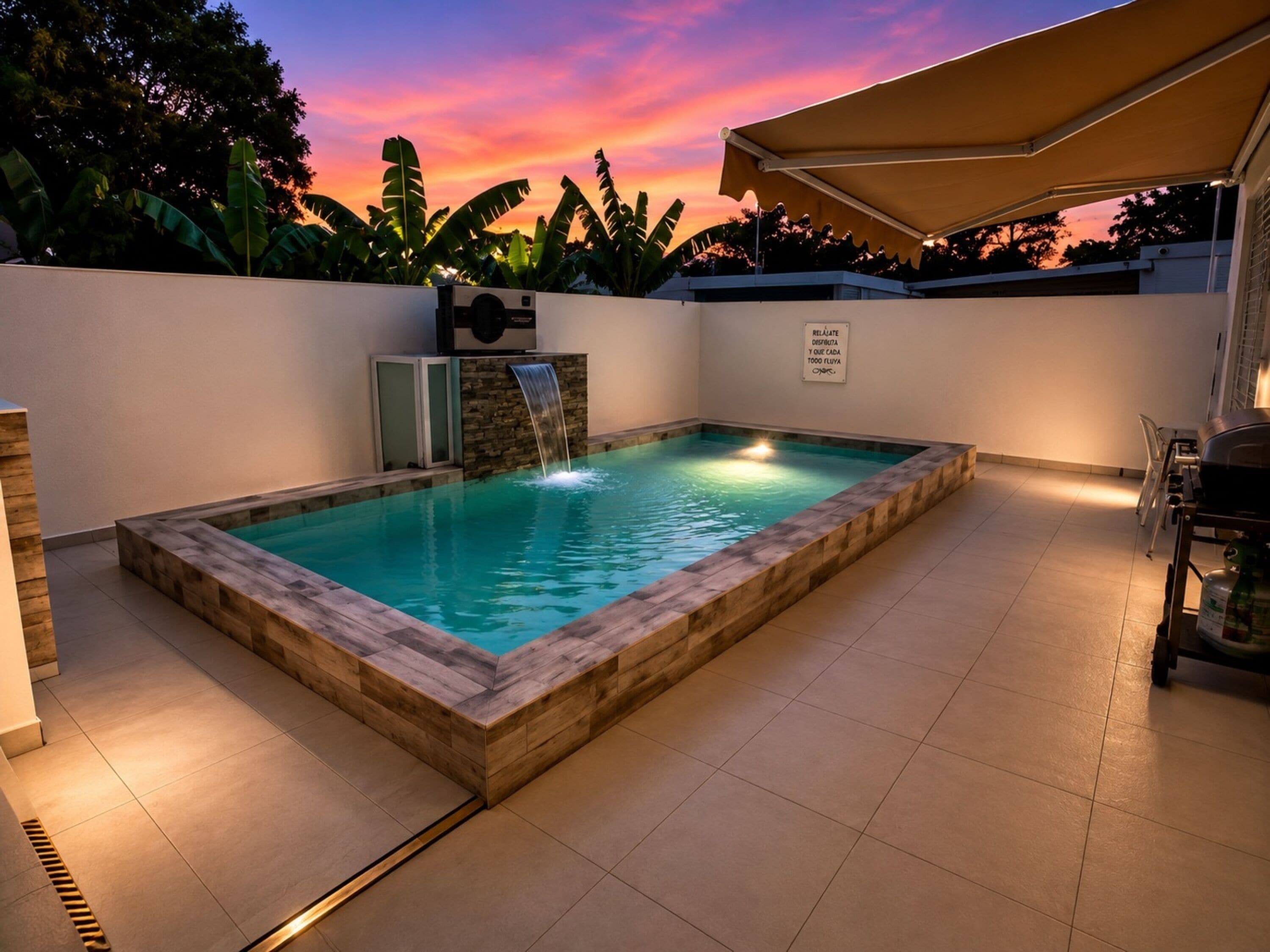 Ein rechteckiger Pool mit Wasserfall, umgeben von einer Holzterrasse und einer gefliesten Terrasse.