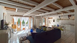 Amplia sala de estar con un sofá, una mesita y un televisor. Cuenta con una zona de cocina con lavadora y un comedor con mesa y sillas.