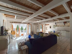 Ein großzügiger Wohnbereich mit einer Couch, einem kleinen Tisch und einem Fernseher. Es gibt eine Küchenzeile mit einer Waschmaschine und einen Essbereich mit Tisch und Stühlen.