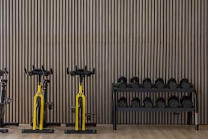 Ein Fitnessraum mit Trainingsgeräten, darunter Fahrradergometer und ein Gewichthebelständer.