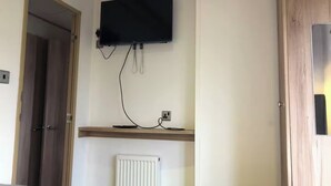 Una habitación de hotel con cama, televisor montado en la pared, radiador y puerta de madera.