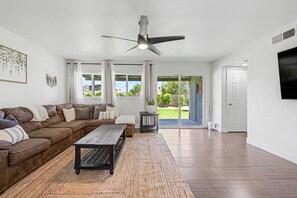 A living room with a brown leather sofa, a wooden coffee table, and a ceiling fan. - Bluefield Garden - Serene Desert Landscape with Fire Pit (Phoenix)