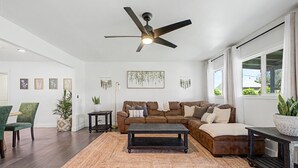 Un salon avec un canapé en cuir marron, une table basse sombre, un fauteuil vert, un lampadaire et un ventilateur de plafond.
