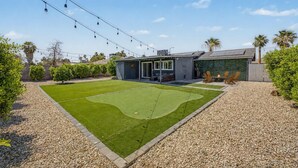 Un jardin avec une pelouse, un espace patio et une maison au design moderne.