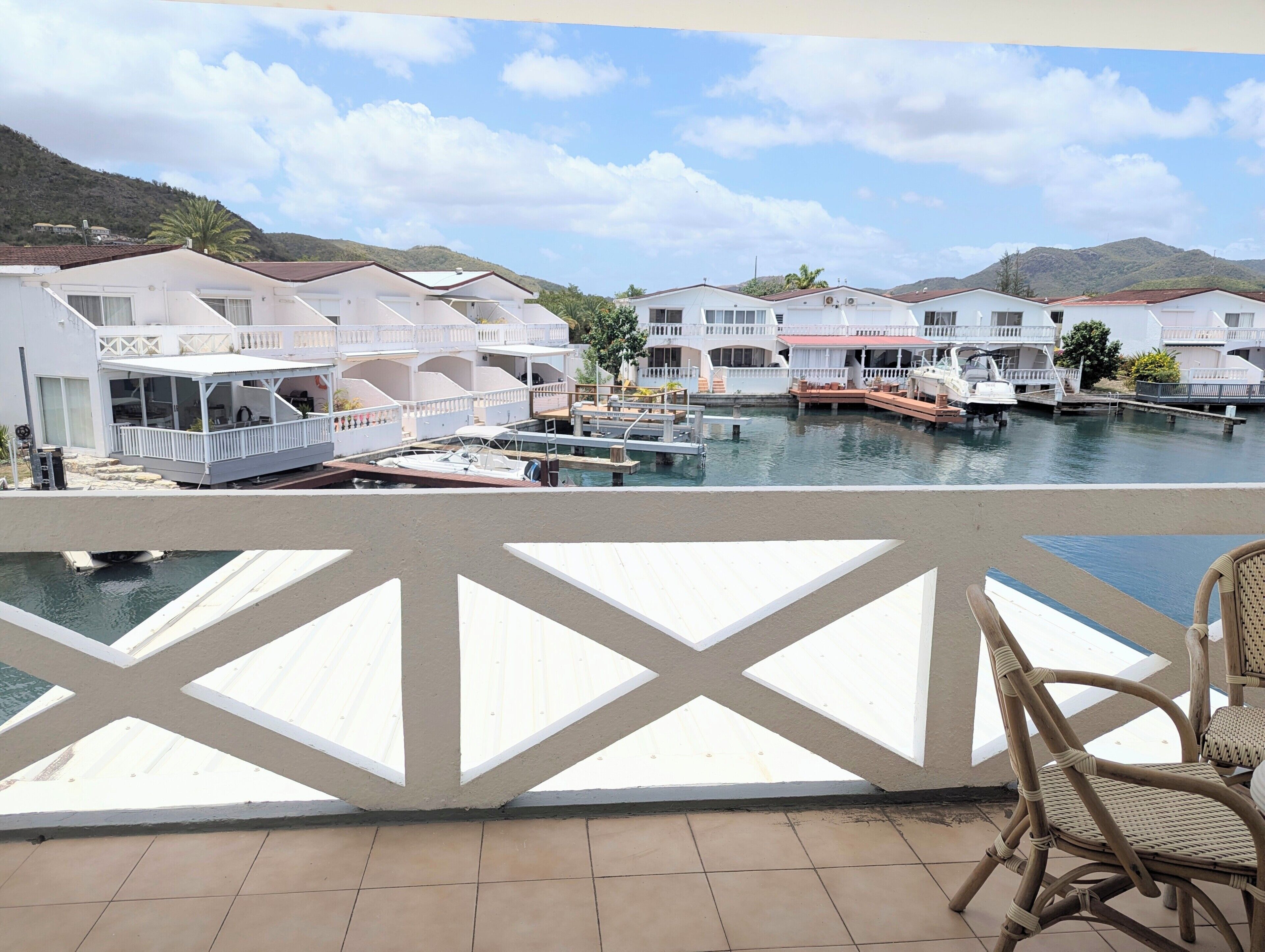 A waterfront property with multiple white buildings, a dock with boats, and a balcony with a chair.