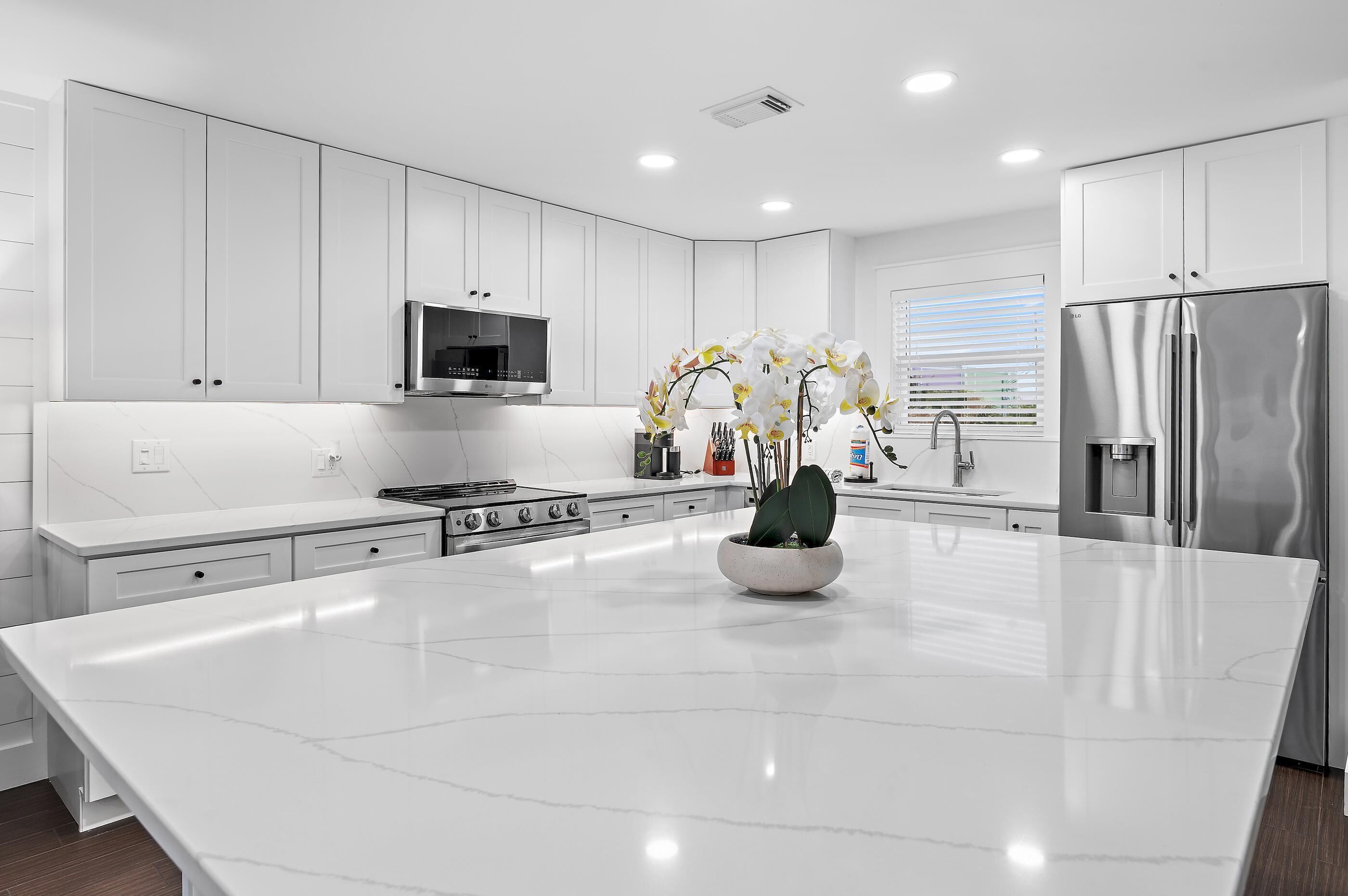 A modern kitchen with white cabinetry, a central island, stainless steel appliances, and a decorative orchid arrangement.