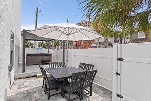 Une terrasse extérieure avec une table et des chaises, un barbecue et une clôture blanche.