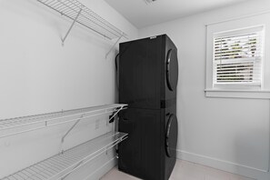 Une buanderie avec un appareil électroménager noir, des étagères en métal et une fenêtre avec des stores.