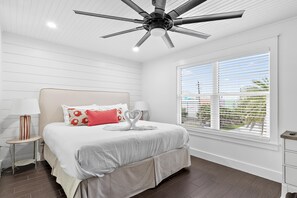 A bedroom with a bed, a ceiling fan, a window with blinds, and a nightstand with a lamp. - Emerald Hideout (Miramar Beach)