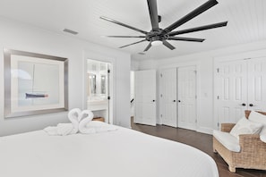 A bedroom with a bed, a ceiling fan, white doors, and a wicker chair. - Emerald Hideout (Miramar Beach)