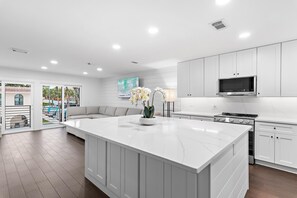 A modern kitchen with white cabinetry, a large island, and a flat-screen TV. - Emerald Hideout (Miramar Beach)